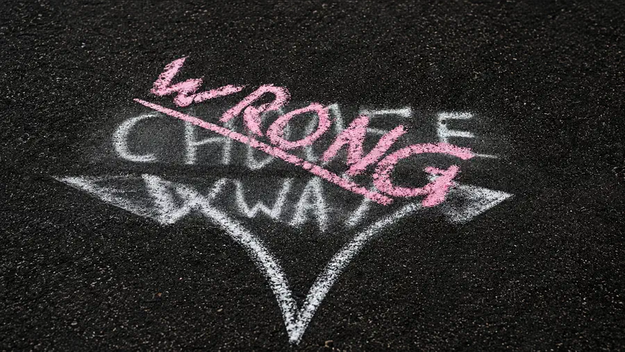 Chalk graffiti on dark pavement showing the words “Wrong Way” crossed over a large white directional arrow