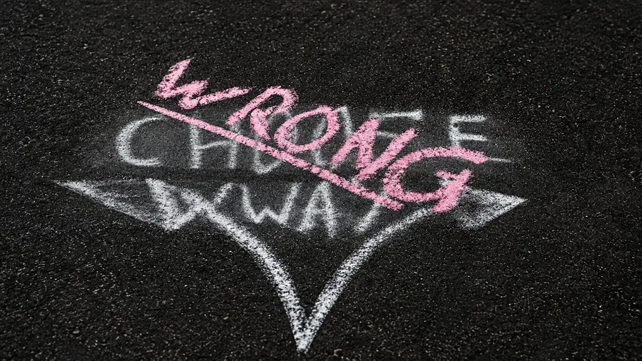Chalk graffiti on dark pavement showing the words “Wrong Way” crossed over a large white directional arrow