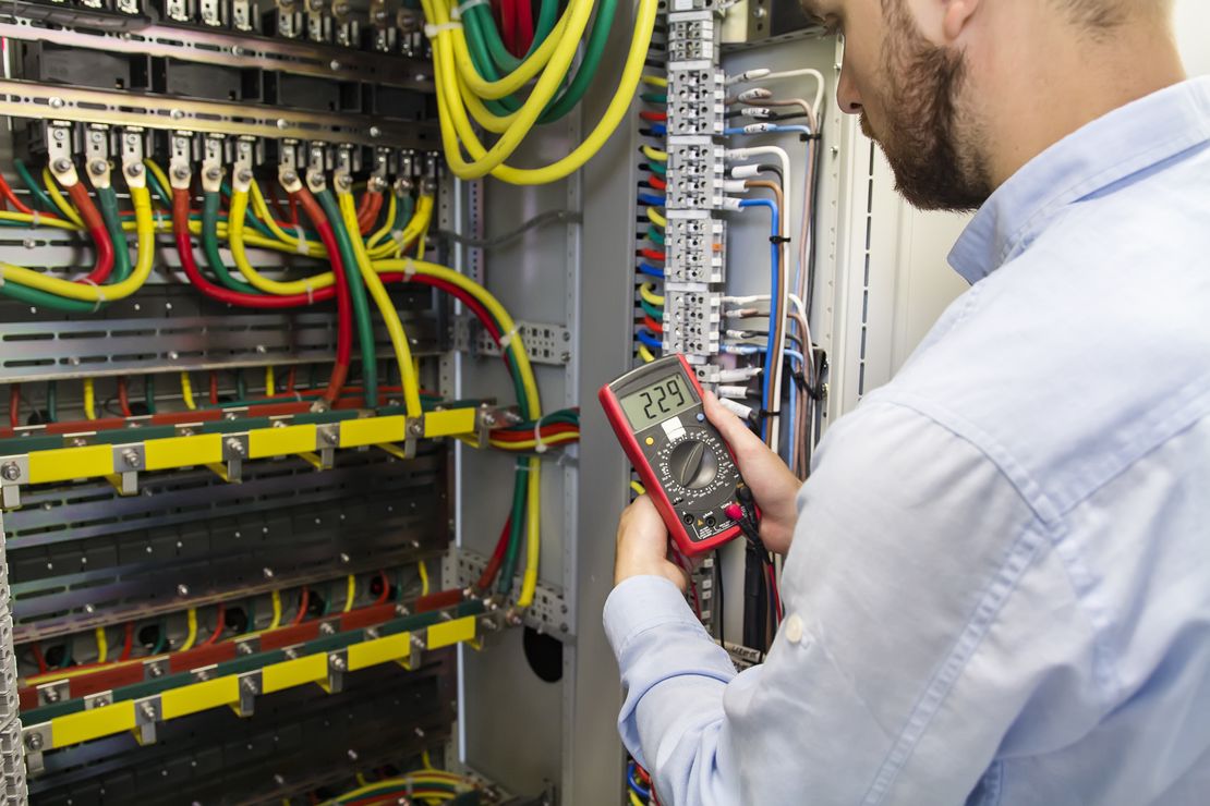 Electrician testing a control panel with a multimeter, managed using Cinderblock job management software.