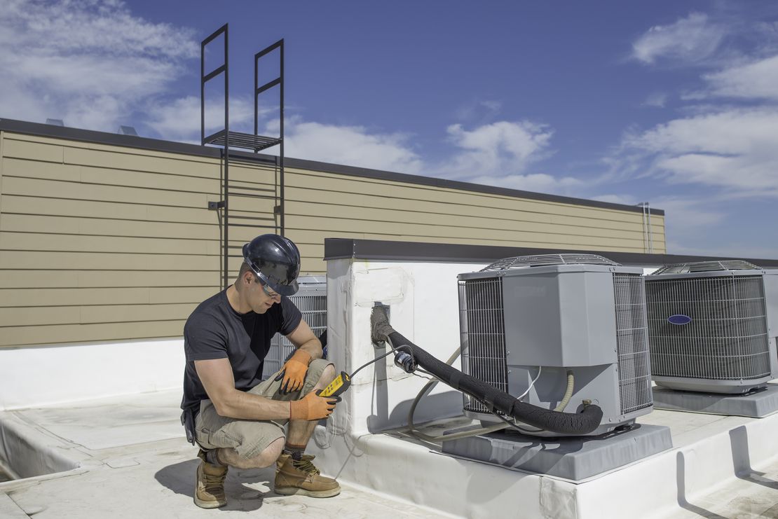 HVAC technician inspecting a rooftop AC unit while managing the job with Cinderblock job management software.
